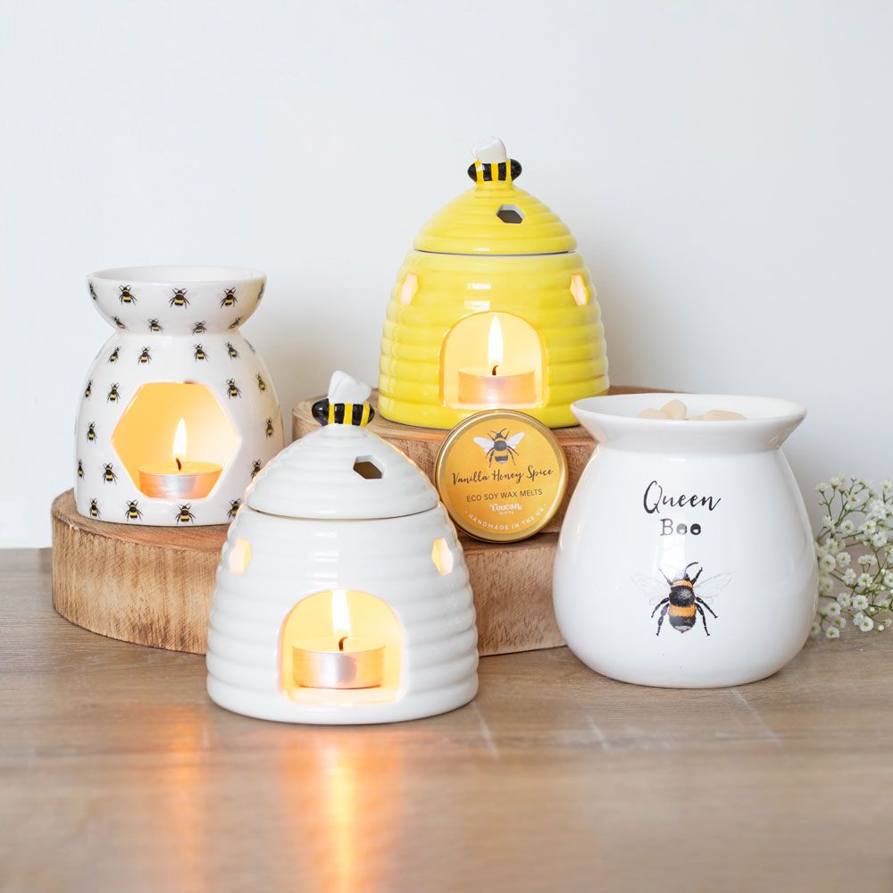 Collection of Bee Themed Oil/Wax Burners with Bee Motif, Displayed on Wooden Surface with Tree Slices, White Flowers, and Wax Melts Tin